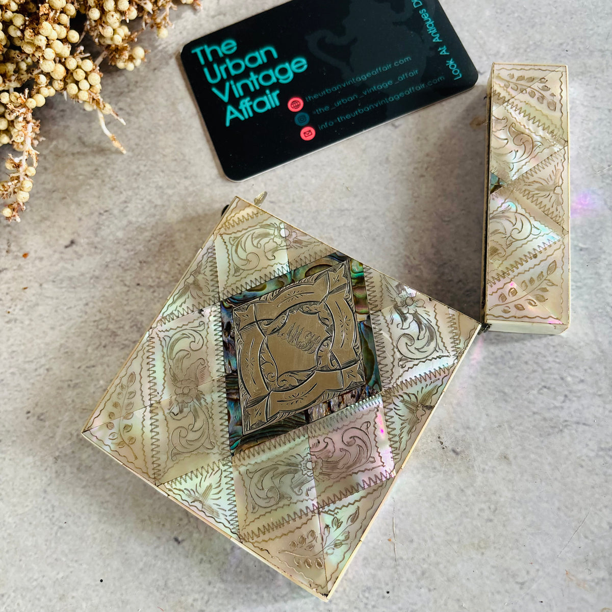 A Rare Antique Mother Of Pearl And Sterling Silver Calling Card Case shown open with a gold-toned mirror insert, alongside a matching closed case and a black business card for 'The Urban Vintage Affair' on a textured light surface.