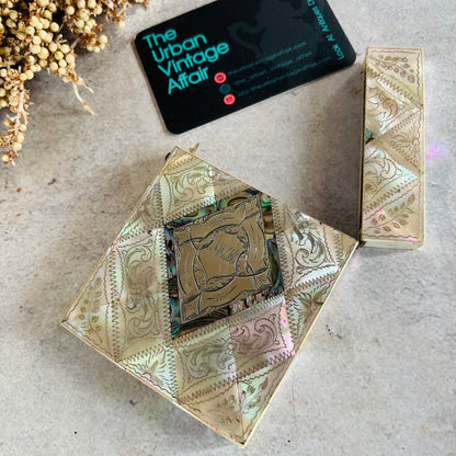 A Rare Antique Mother Of Pearl And Sterling Silver Calling Card Case shown open with a gold-toned mirror insert, alongside a matching closed case and a black business card for 'The Urban Vintage Affair' on a textured light surface.