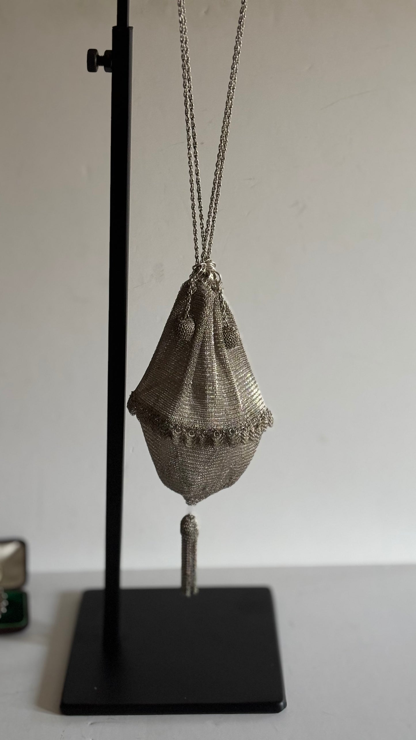 silver chain mail bag with tassels hanging from a stand against a plain background