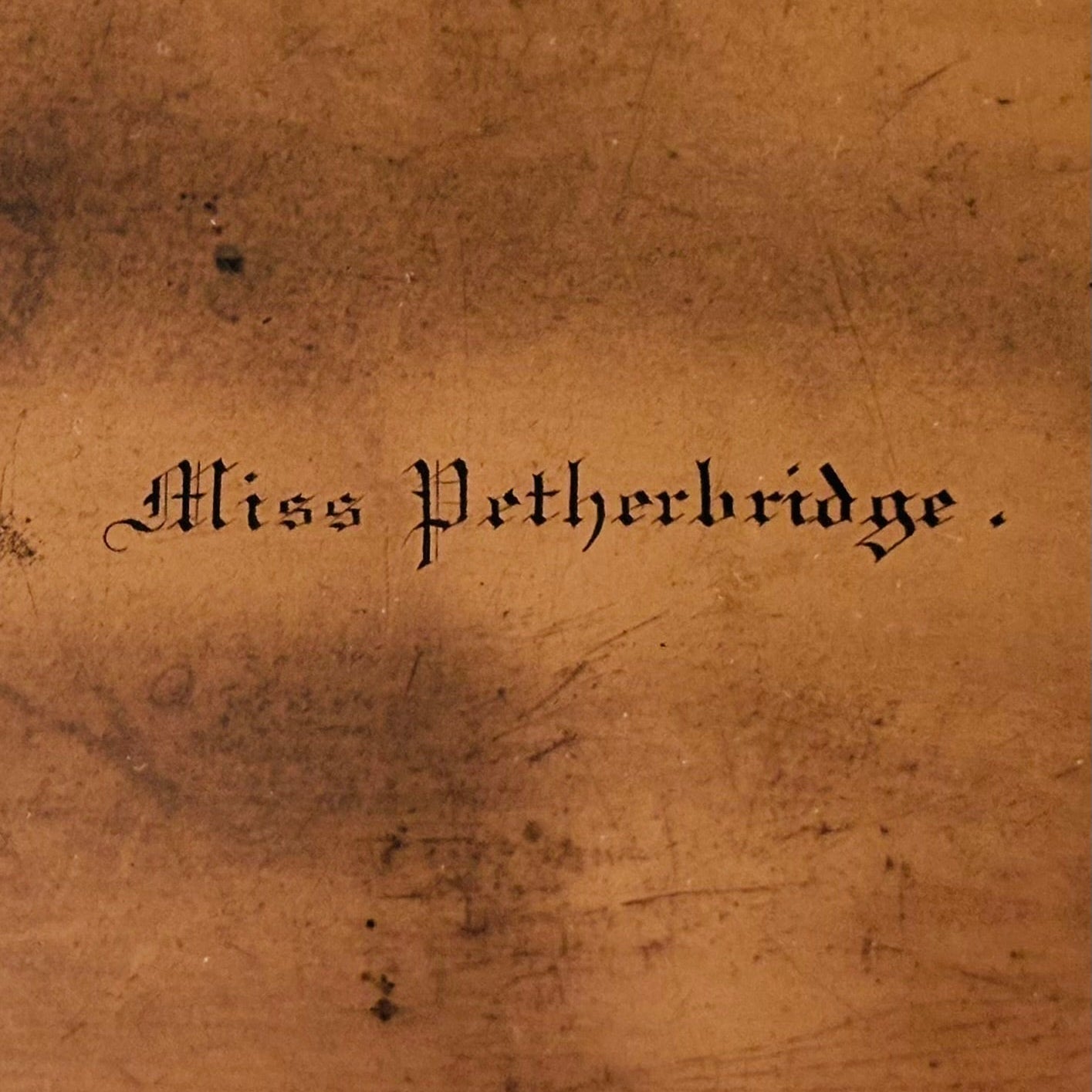 A close-up of a copper printing plate with the cursive text 'Miss Petherbridge.' printed in black in the center.