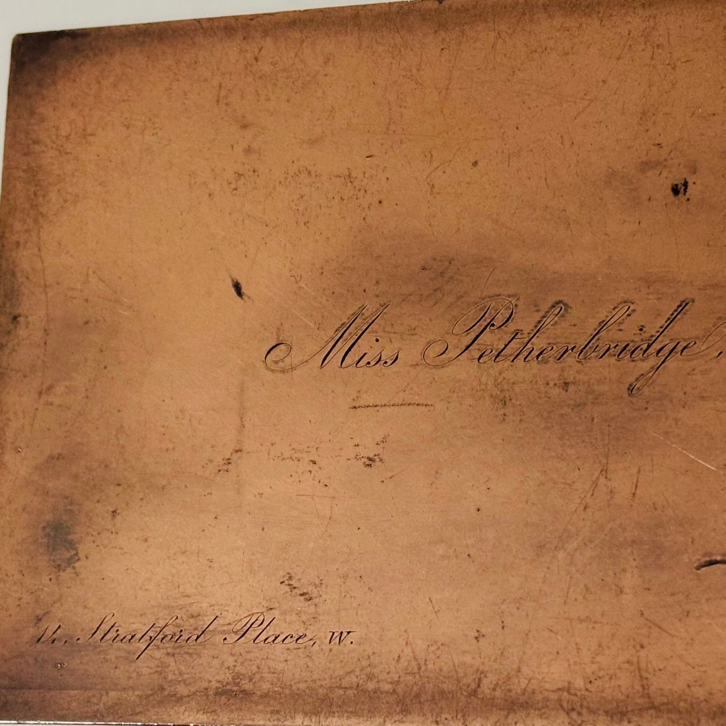 A close-up of a copper printing plate with cursive handwriting reading 'Miss Ptherbridge' and '144 Stratfford Place, W.' on a light gray background.