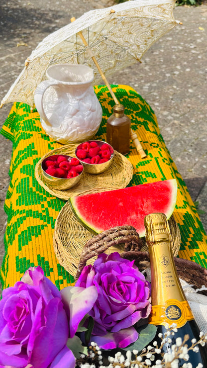 Table with watermelon, raspberries, and a bottle of champagne on a colorful tablecloth.