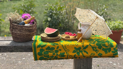 Outdoor setting with a colorful tablecloth, watermelon, and decorative items on a bench.