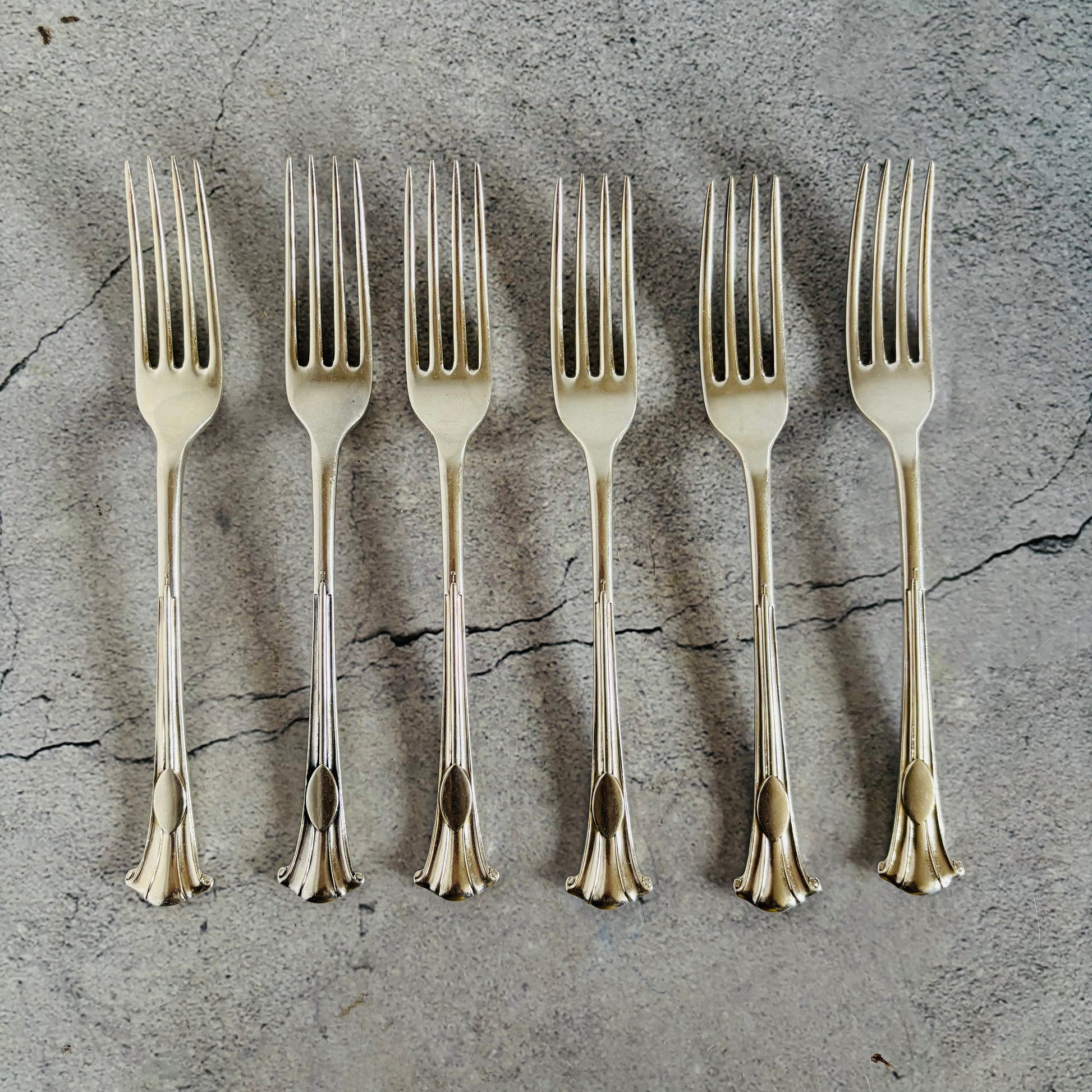 Set of six silver forks on a textured grey surface