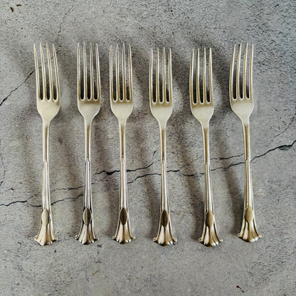 Set of six silver forks on a textured grey surface