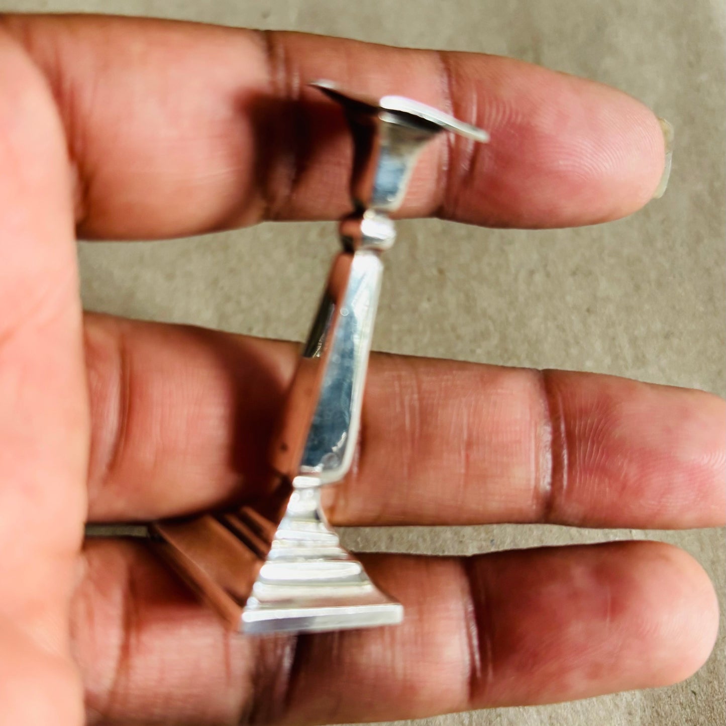 Small Antique Silver Miniature Candlestick held between fingers against a neutral background