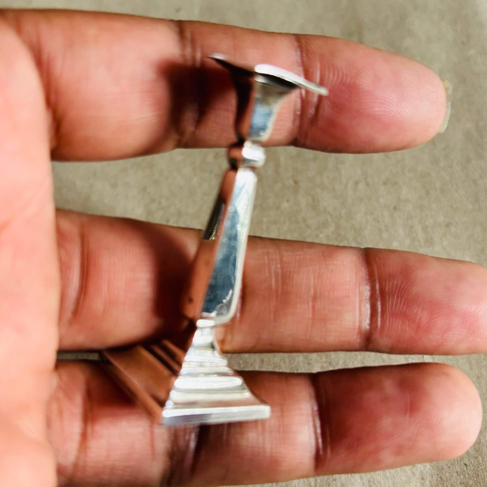 Small Antique Silver Miniature Candlestick held between fingers against a neutral background