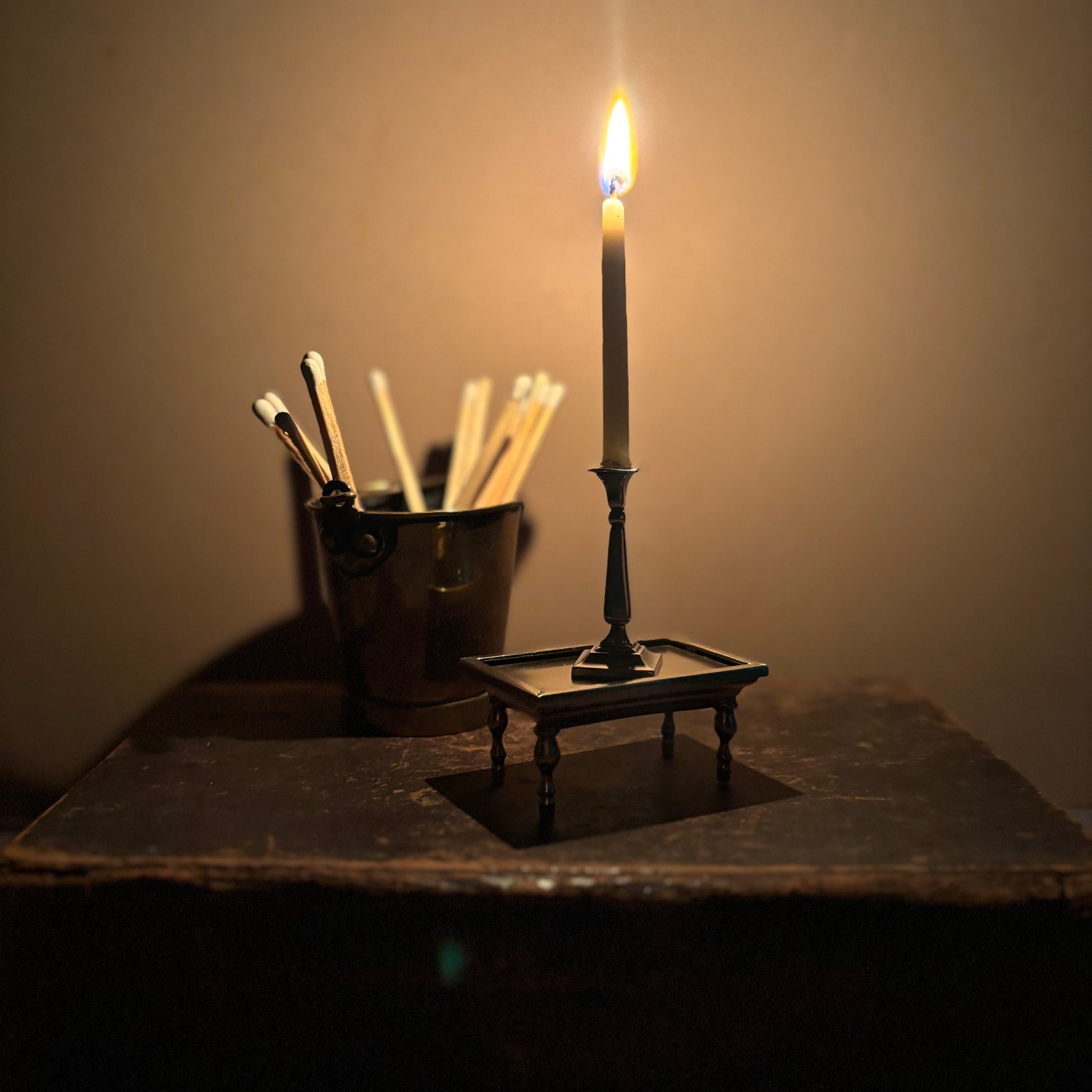 lit Candle in a holder on a surface with matches in the background