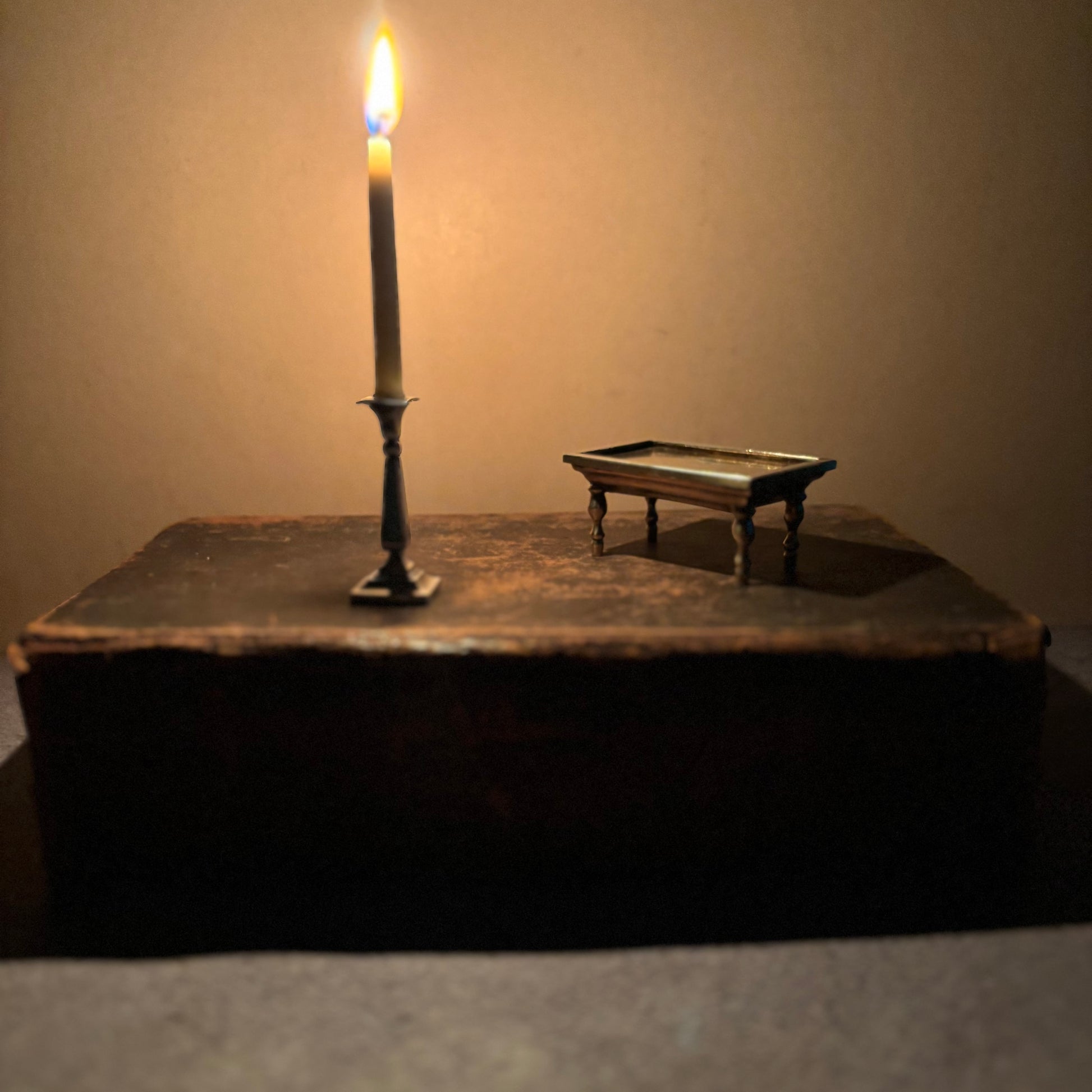 Miniature candle on a stand next to an old book with a miniature table on