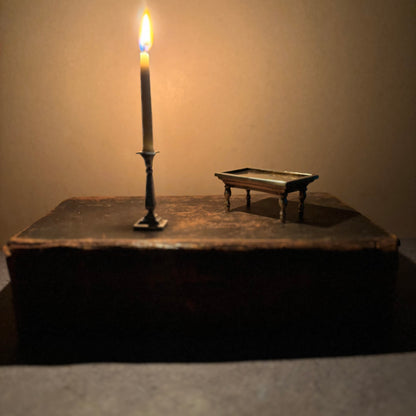 Miniature candle on a stand next to an old book with a miniature table on
