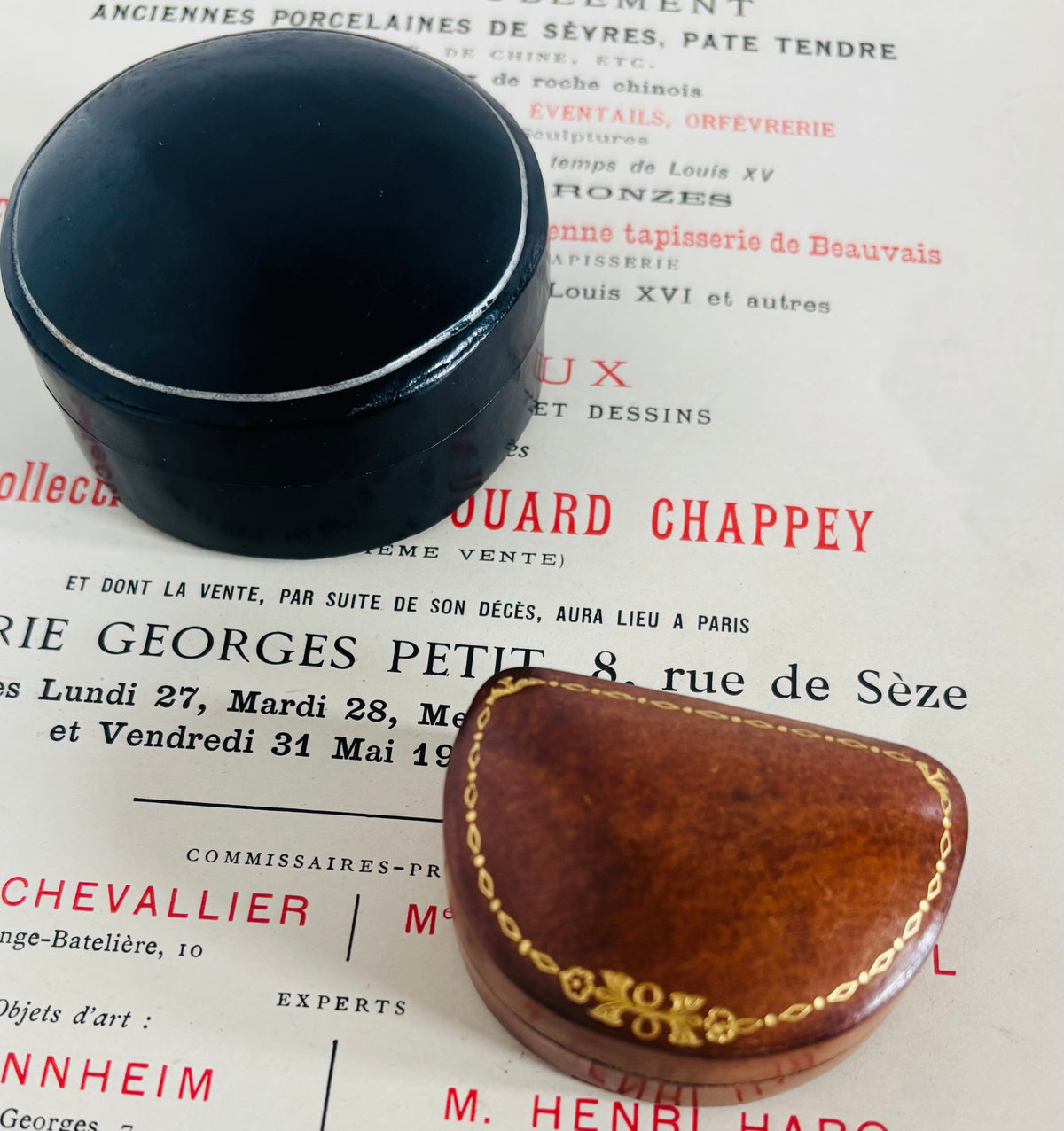 A vintage art object box with a black lid and a brown wooden case with gold trim, displayed on top of a printed antique catalog from Chevalier M.