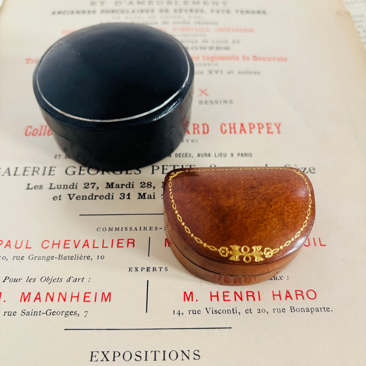 Two vintage jewelry boxes on a paper background: a round black lacquered box and an oval brown wooden box with a gold chain link detail and '100% ORCI' inscription.