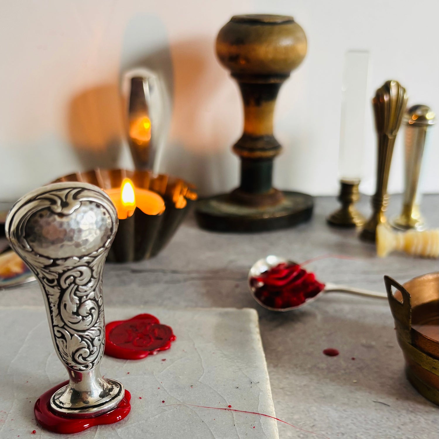 Decorative silver stamp with red wax seal on a stone surface, surrounded by antique wax seal stamps.