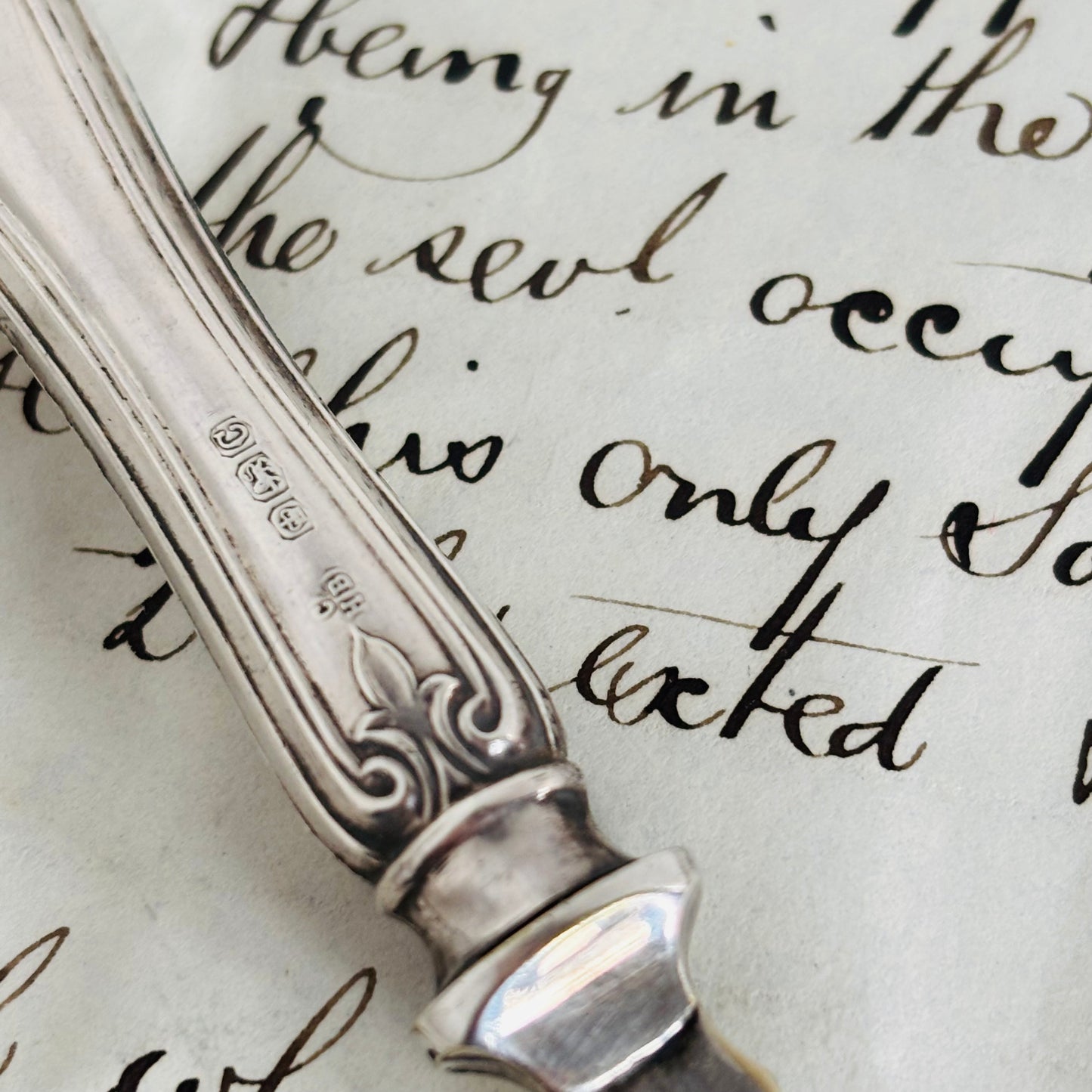 Silver spoon handle with intricate design on a piece of paper with cursive text