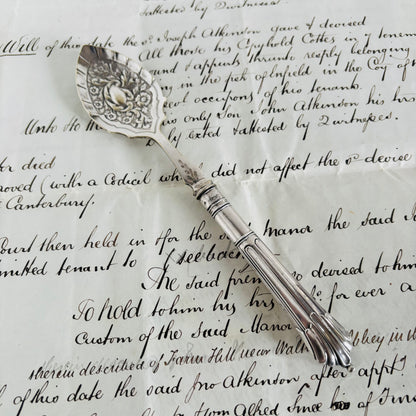 Decorative silver spoon on top of an old document with cursive writing.