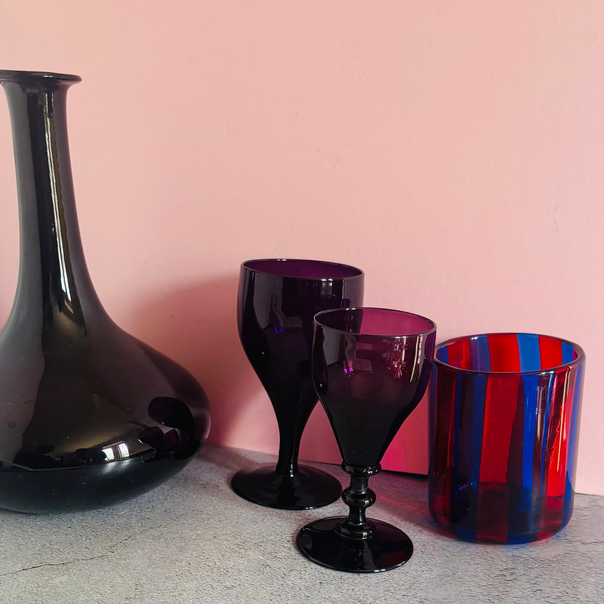 Amethyst wine glassware and a red and blue striped glass against a pink background