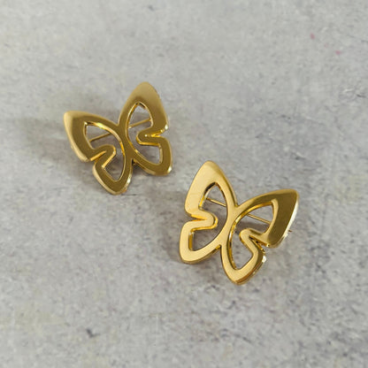 Gold butterfly earrings on a gray concrete surface
