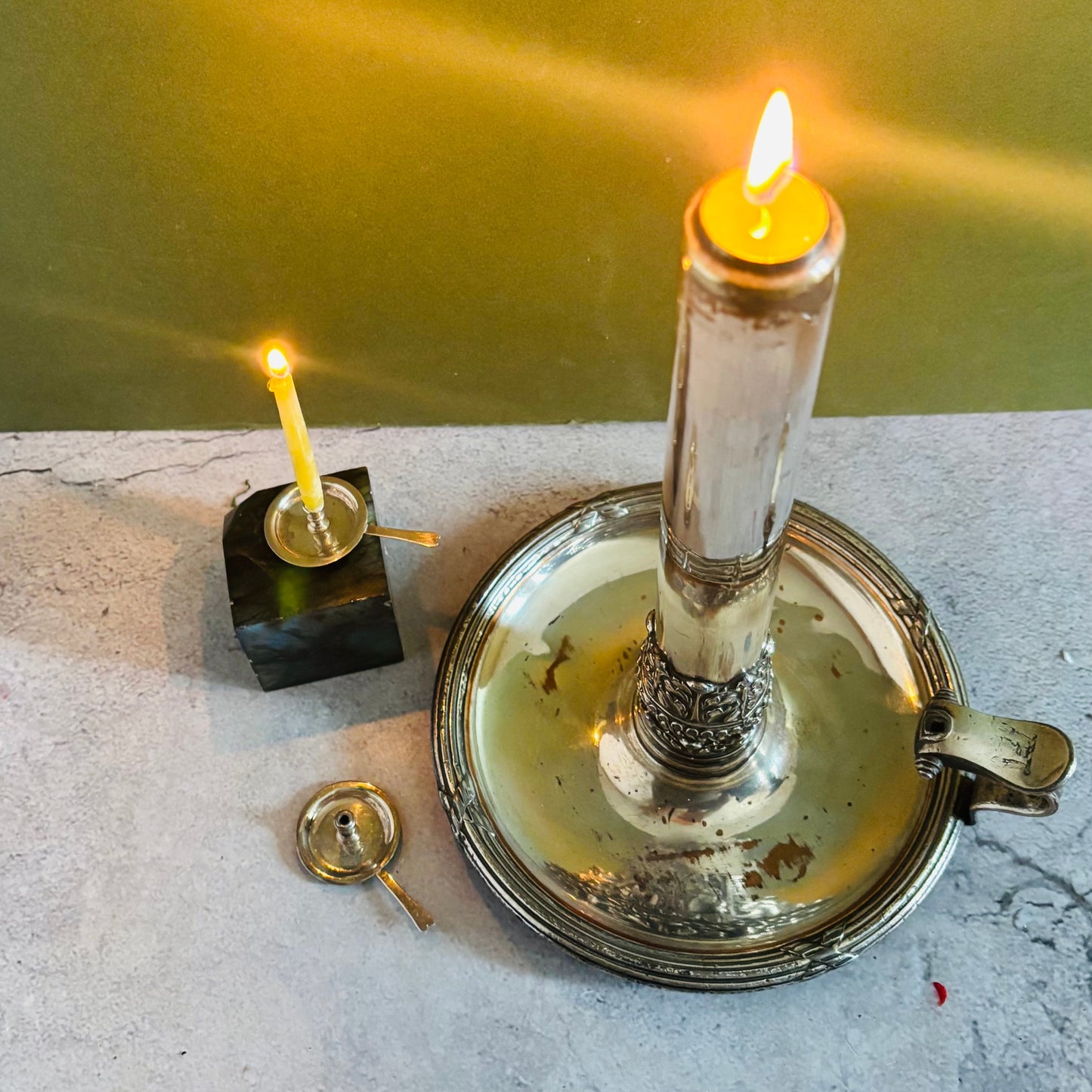Two lit candles on a metal stand against a green wall.