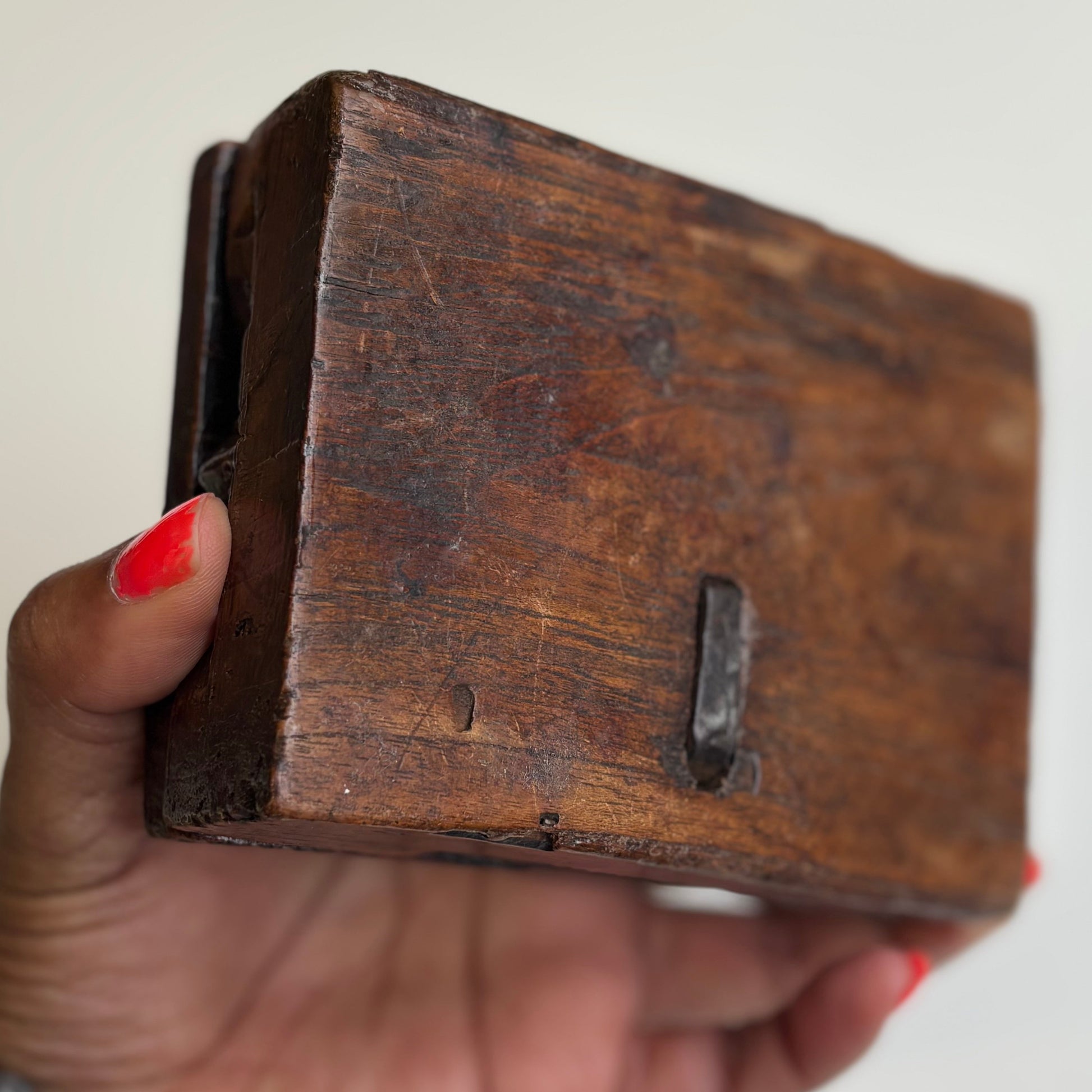 Hand holding a wooden block with a metal component on a plain background