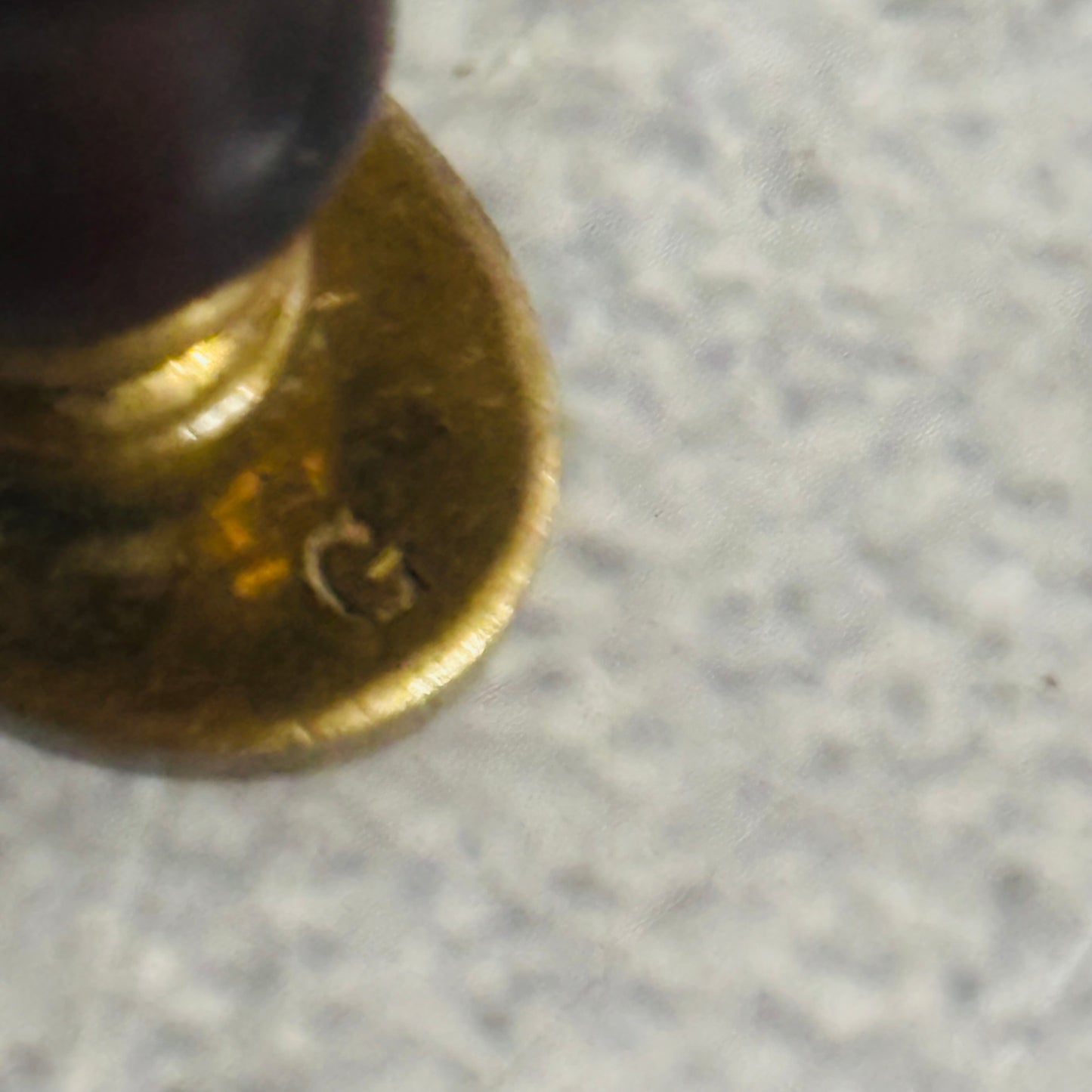 Close-up of a brass seal with 'G' marking on a gray surface