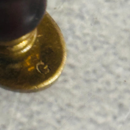 Close-up of a brass seal with 'G' marking on a gray surface