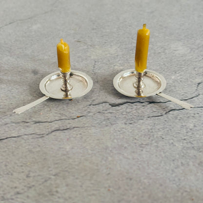 Two miniature candle holders with yellow candles on a grey concrete surface