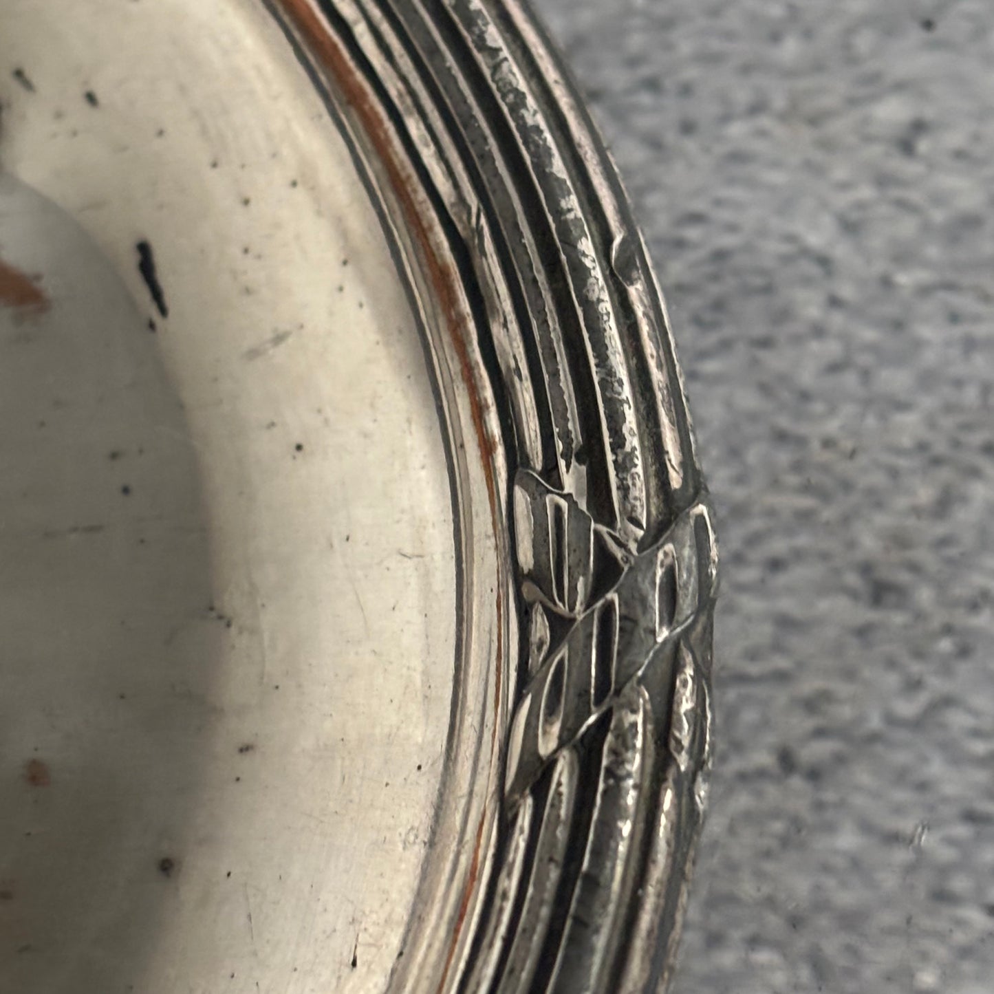 Close-up of a silver decorative plate with intricate patterns on a textured surface.