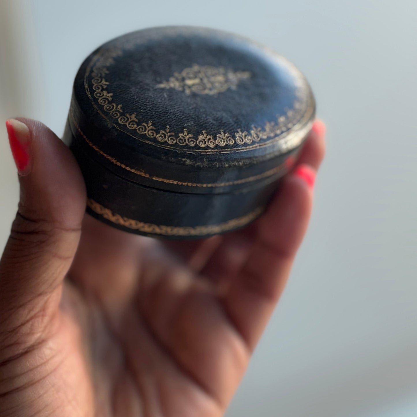 Hand holding a small round black container with gold detailing against a light background