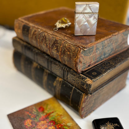 Stack of old books with decorative boxes on a white surface