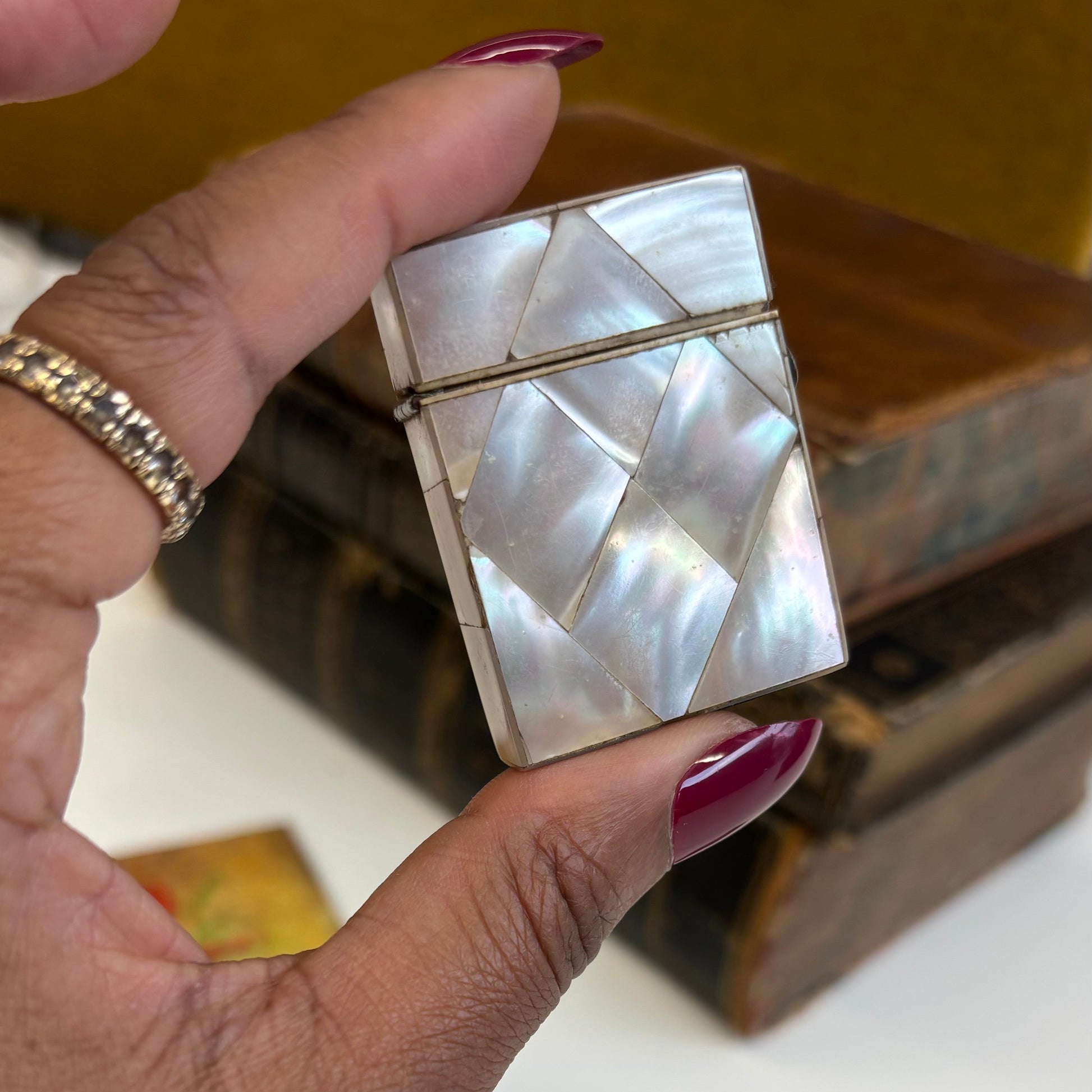 Hand holding a decorative vesta with a shell pattern, with a blurred antique books in the back ground.