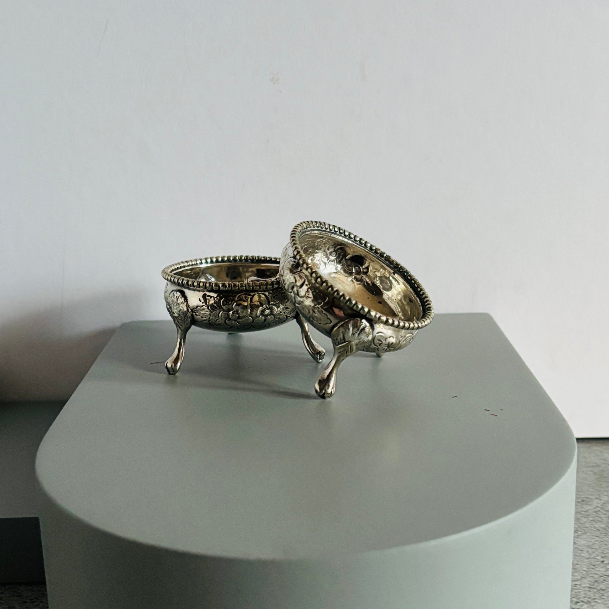 Decorative silver salts on a grey pedestal against white background