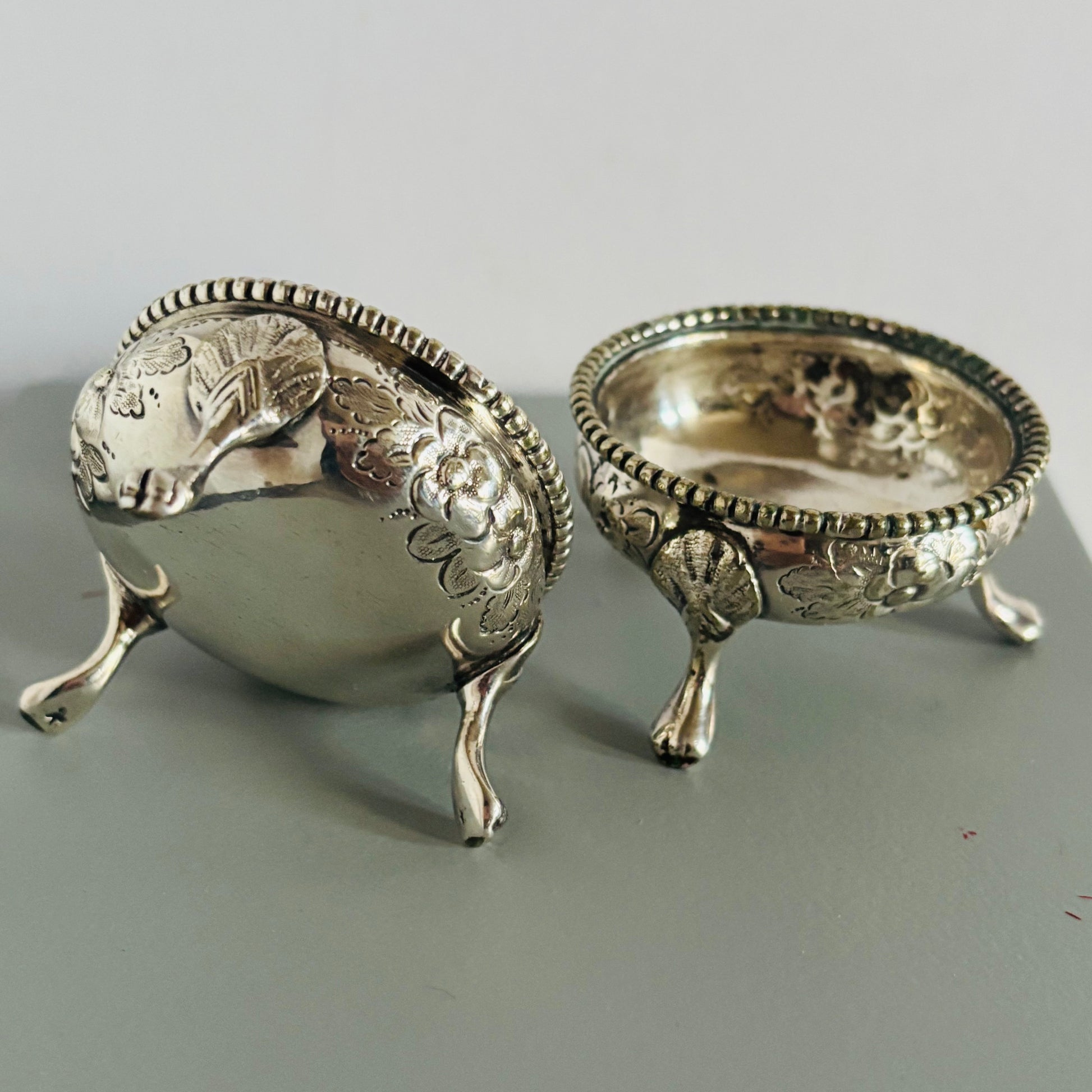 Two silver salt cellars on a grey surface