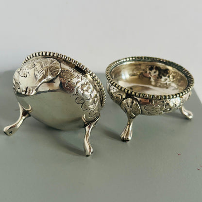 Two silver salt cellars on a grey surface
