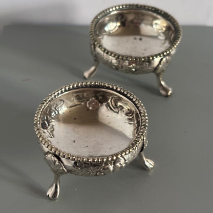 Two ornate silver candle holders on a gray surface