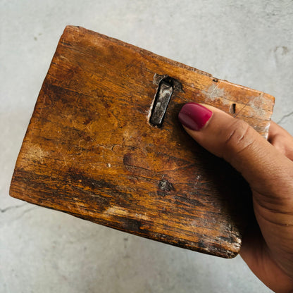 Hand holding a worn wooden block with a metal clip on a light gray background