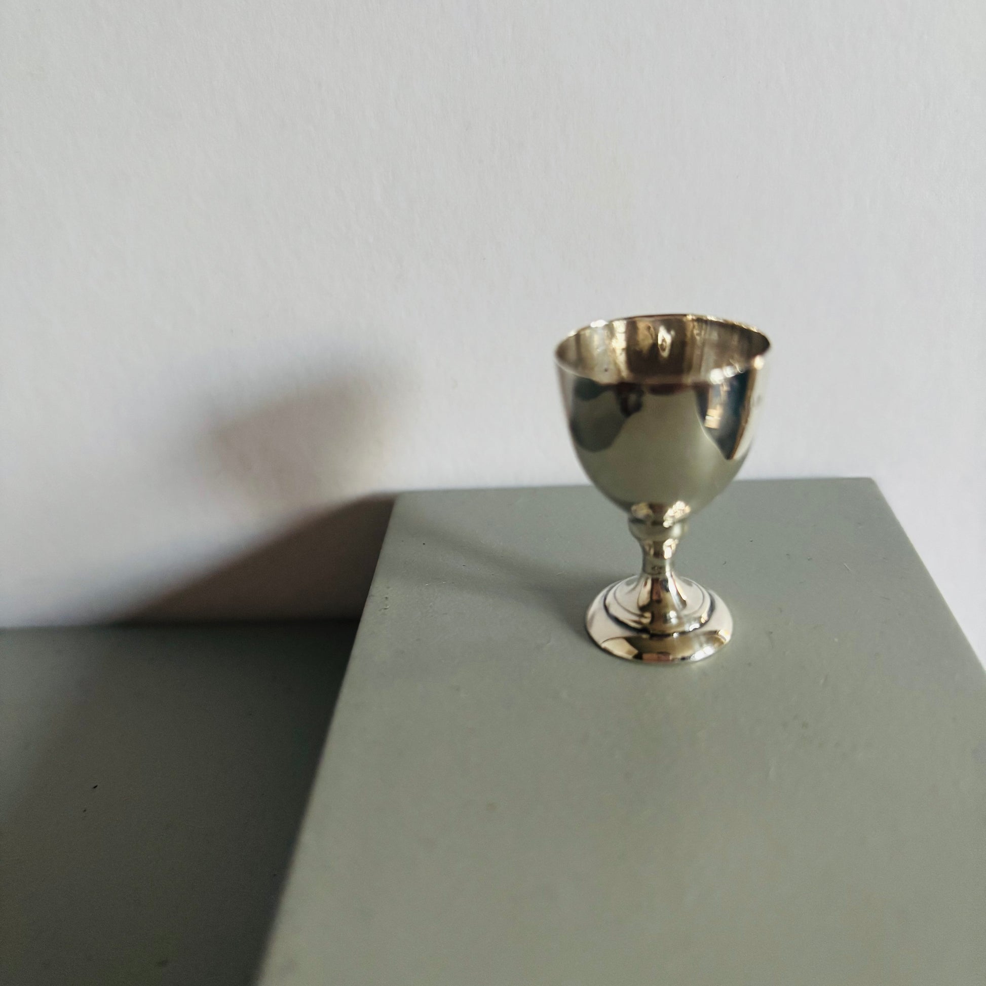 Silver miniature goblet on a gray surface with a white background
