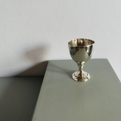Silver miniature goblet on a gray surface with a white background