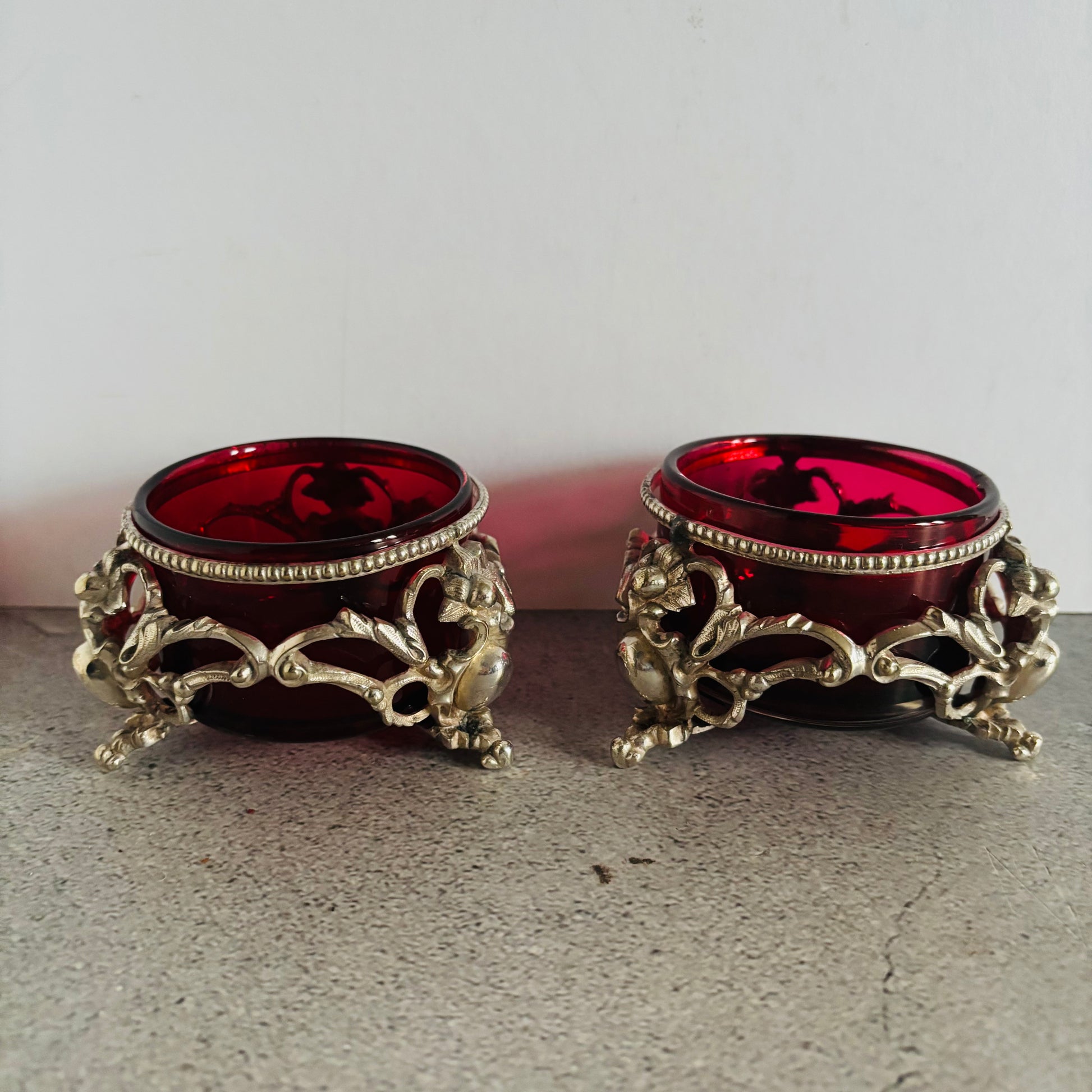 Two ornate candle holders with red glass inserts on a neutral background