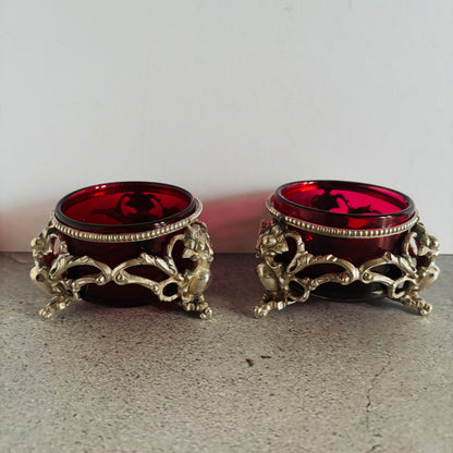 Two ornate candle holders with red glass inserts on a neutral background