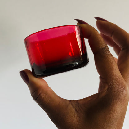 Hand holding a red glass container against a white background