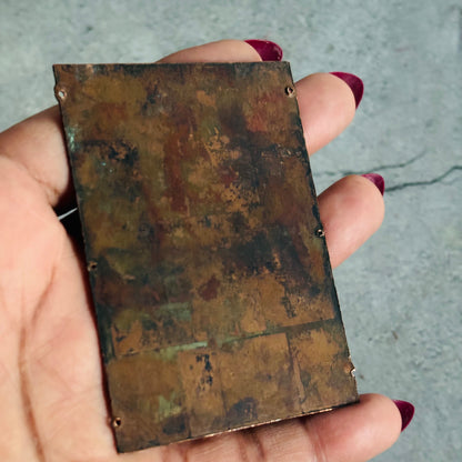Rust-colored metal plate held by a hand with red nail polish against a gray background