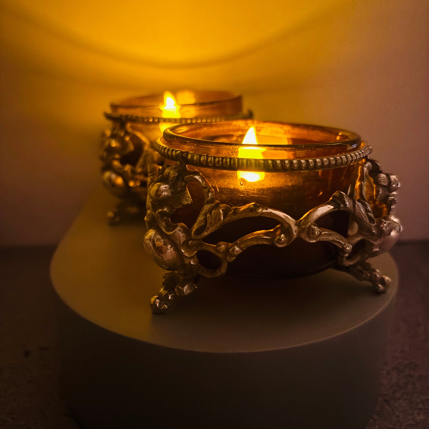 Two lit candles in Ornate Antique Silver Salt cellars with a warm glow