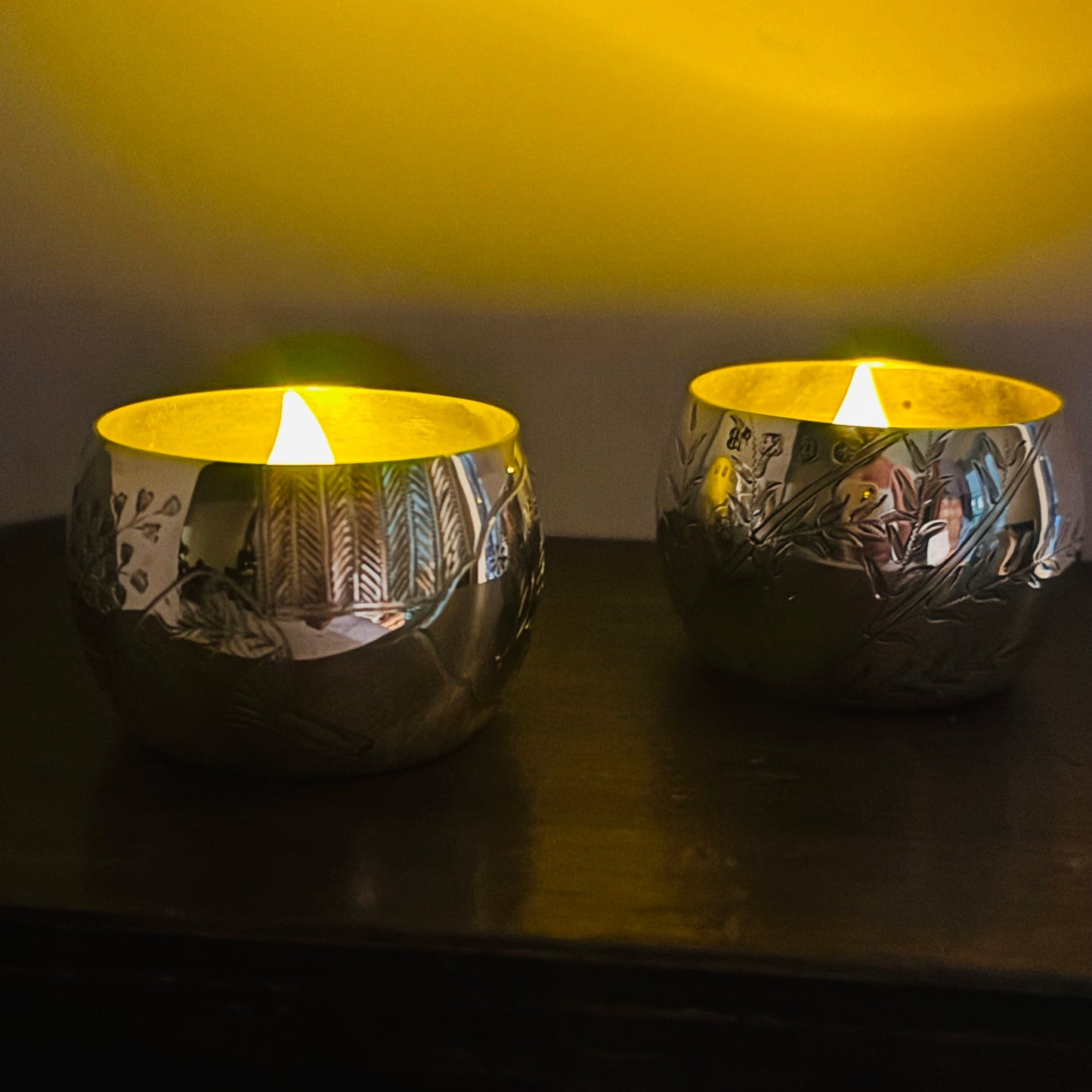 Two Victorian Engraved Silver Saltcellars used as candle holders with lit candles on a wooden surface