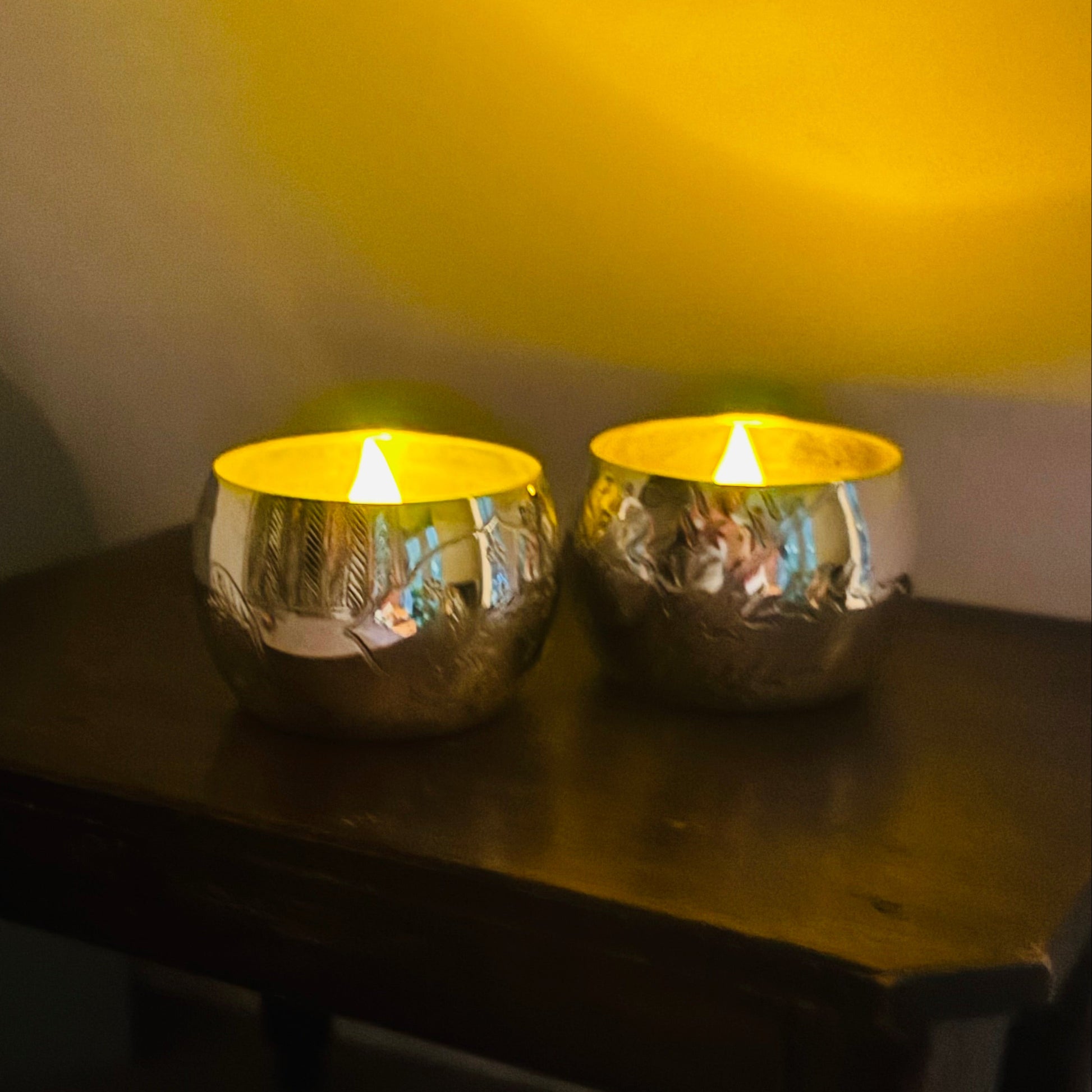 Two Victorian Engraved Silver Saltcellars used as candle holders with lit candles on a wooden surface