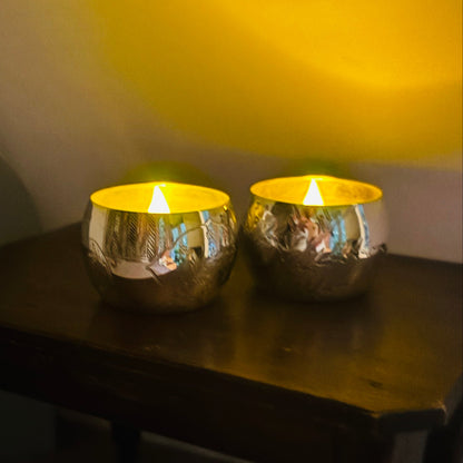 Two Victorian Engraved Silver Saltcellars used as candle holders with lit candles on a wooden surface