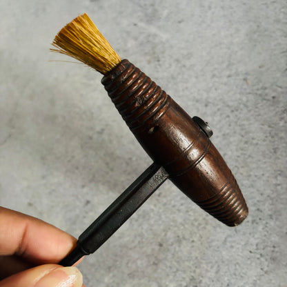 Hand holding a wooden brush with a black handle against a gray background