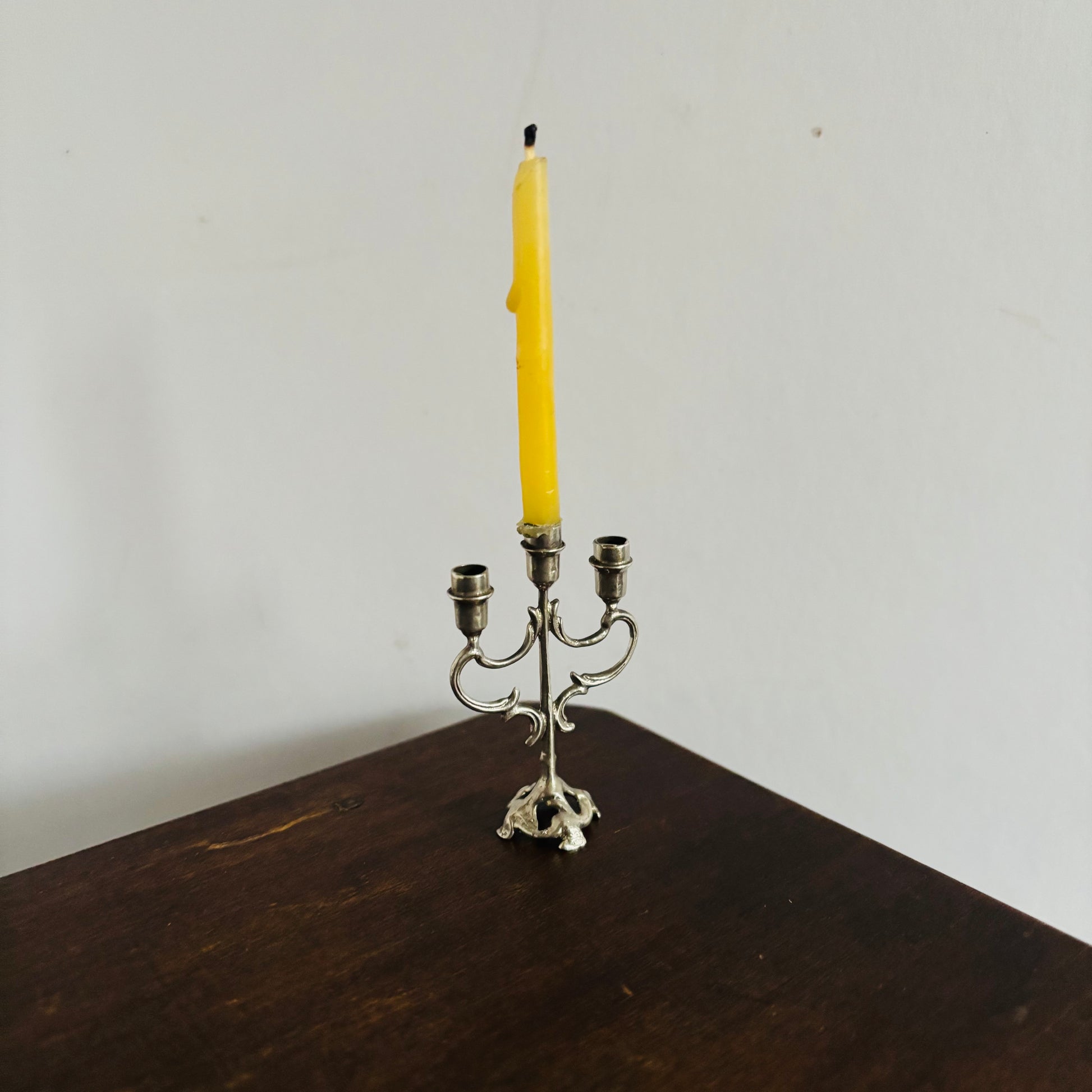 Silver candelabra with a single yellow candle on a wooden surface against a white wall