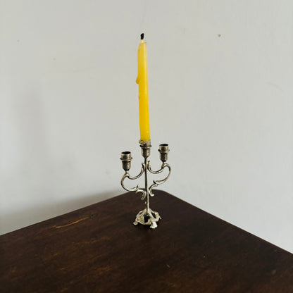 Silver candelabra with a single yellow candle on a wooden surface against a white wall