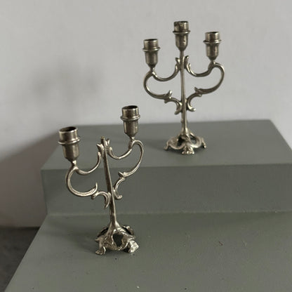 Two silver candelabras on a gray surface with a neutral background