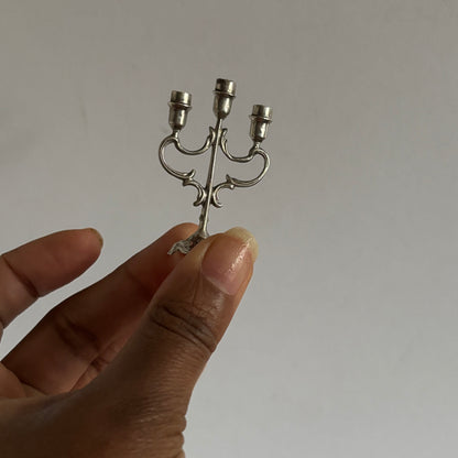 Small silver candelabra held between fingers against a plain background